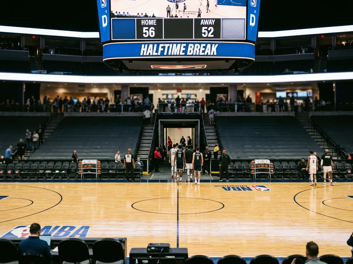 Basketball players on court during halftime break with scoreboard visible